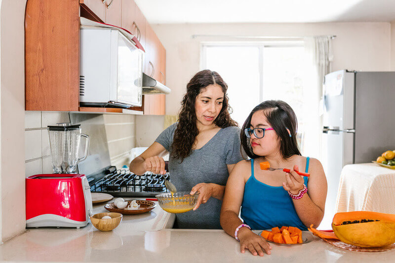 Mother and young disabled teenage daughter cooking in the kitchen together