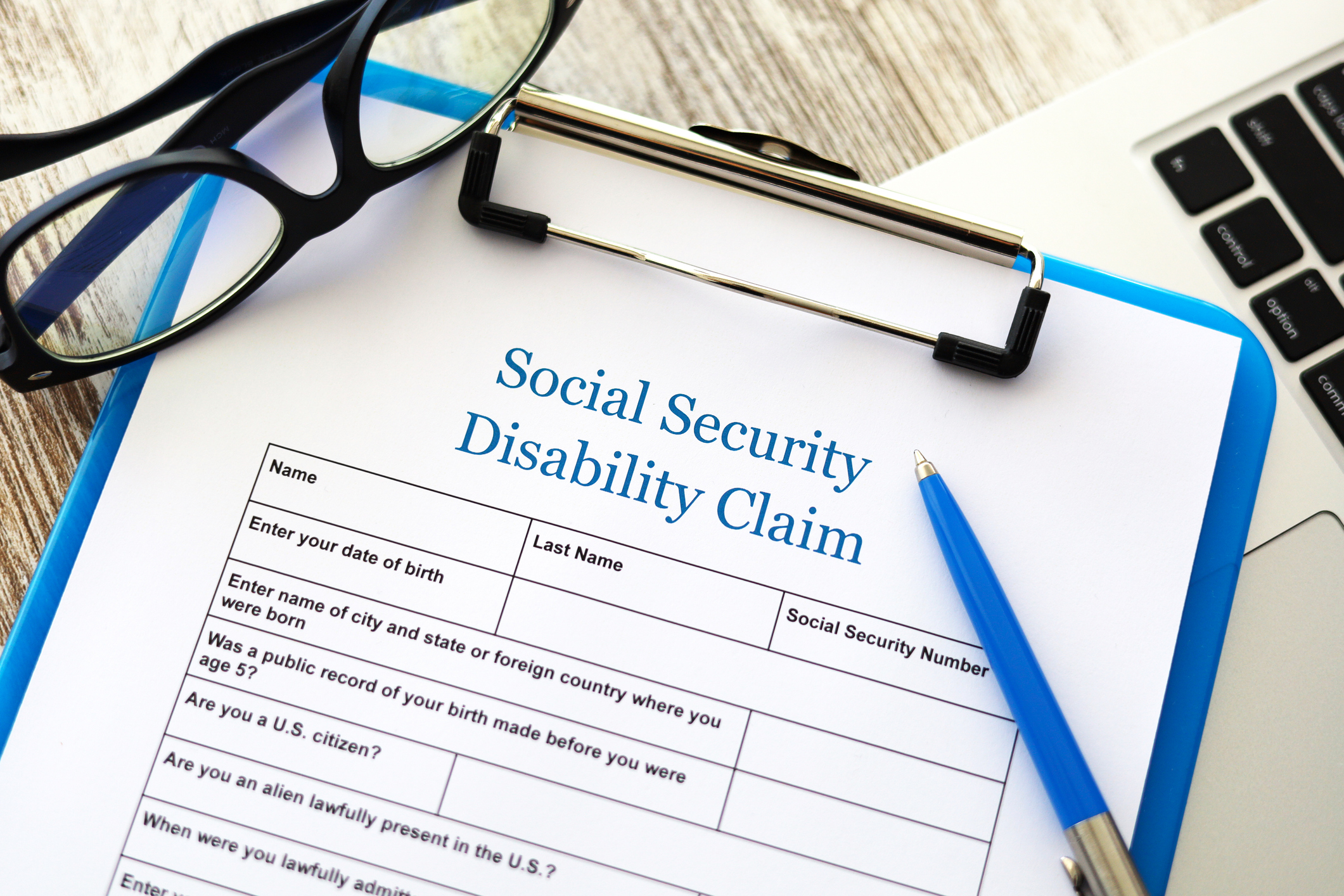Social Security Disability claim form on blue clipboard with pen and glasses sitting on top