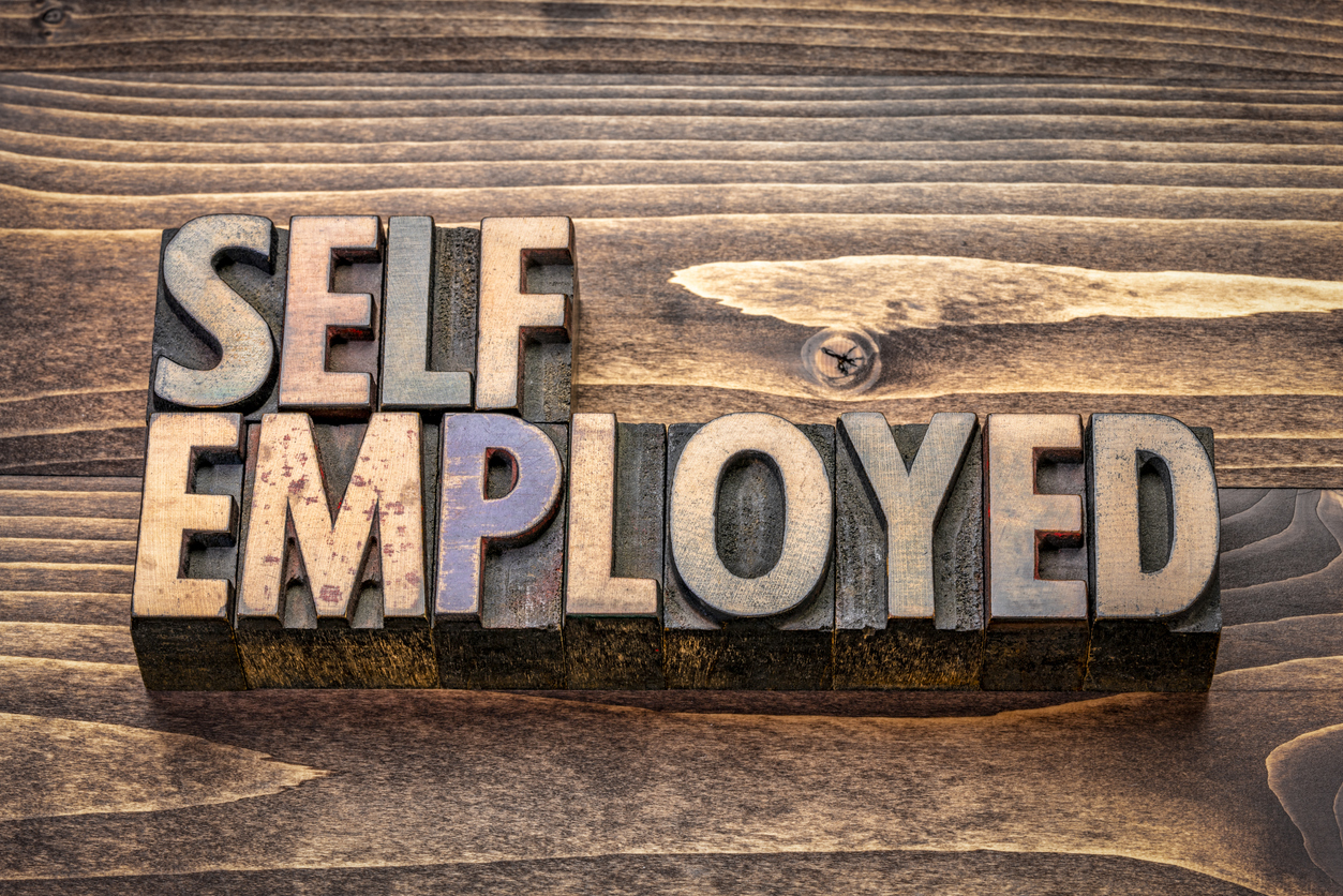 The words "self employed" written out in wood letters on a wood table